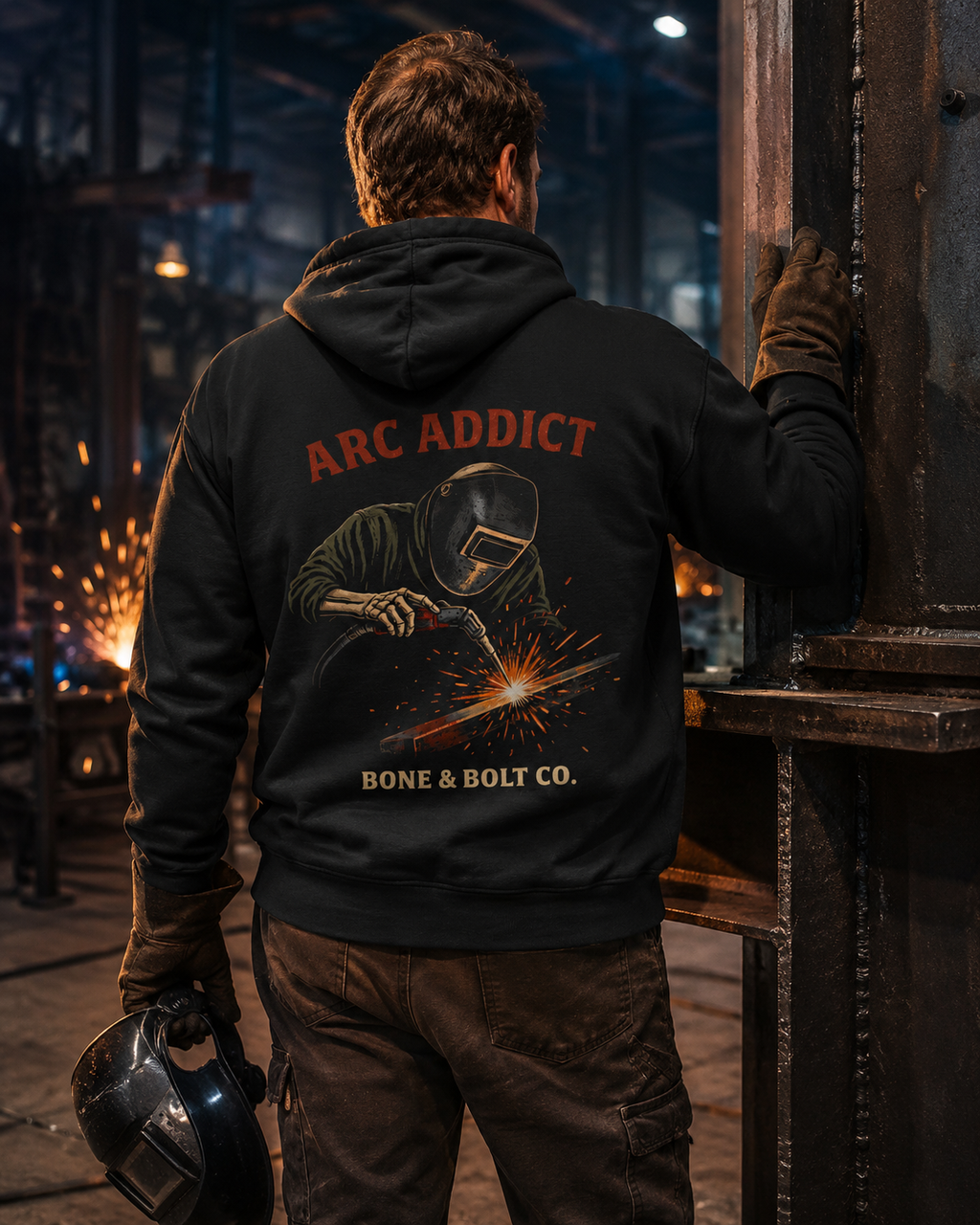 Welder wearing the Arc Addict hoodie in an industrial fabrication shop